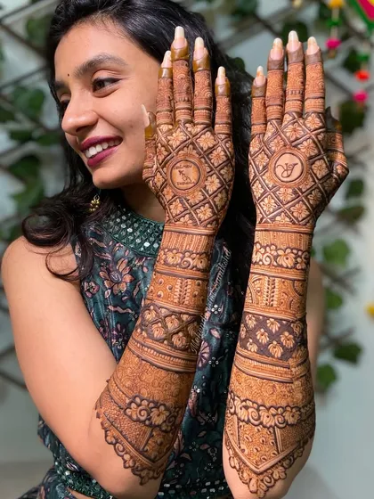 A full view of the bride and her intricate back-of-hand mehendi. The design is personalized with initials and features a classic grid pattern.