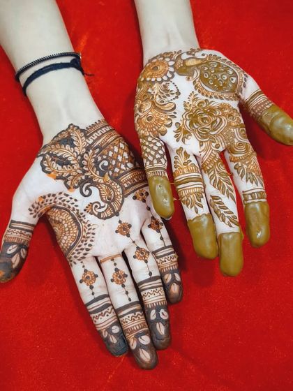 A pair of hands showing two different but complementary designs for wedding guests, one with a paisley motif and the other with floral patterns.