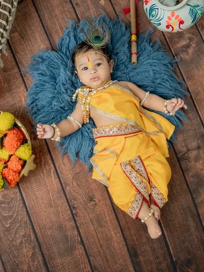 An overhead shot of a baby dressed as Krishna, lying on a soft blue rug. This angle provides a unique perspective and highlights the intricate details of the costume and props.