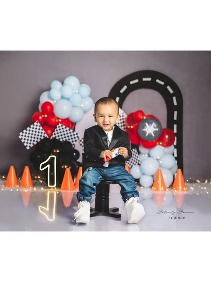 A handsome little racer posing before his cake smash. The themed setup with a neon "1" and traffic cones is so much fun.