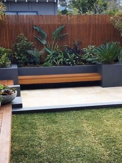 This modern backyard design features a built-in bench integrated into a raised planter bed. The combination of clean lines, wooden elements, and a neat lawn creates a stylish and functional outdoor seating area.