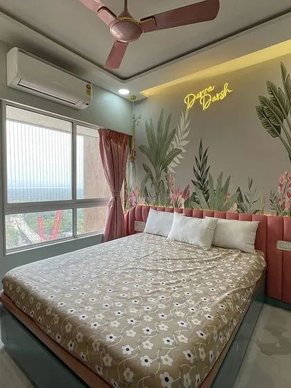A whimsical bedroom featuring a tropical-themed wallpaper and a neon sign that reads "Dream Big." The pink upholstered headboard and matching curtains create a soft and playful atmosphere.