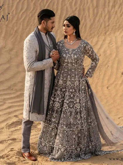 A story of love set against the sands of time. This coordinated couple's ensemble, featuring a grey embroidered gown and a matching sherwani, captures a moment of pure elegance and connection.