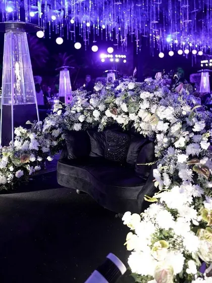 We create stylish and comfortable lounge areas for guests to connect. This chic seating arrangement, enveloped in white florals and set under dramatic purple lighting, provides a sophisticated space for networking at a corporate cocktail party.