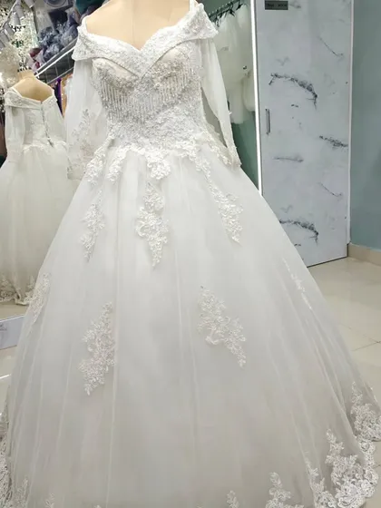 A full-length view of the off-the-shoulder embroidered ball gown. The floral lace appliqués cascade from the bodice down onto the voluminous tulle skirt.