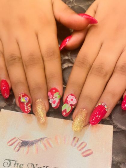 A bright and cheerful set of red almond nails. The design includes gold glitter accents and hand-painted 3D flowers and a flamingo for a fun, summery vibe.