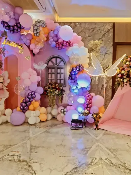 A magical fairy garden created for a birthday celebration. This elaborate setup includes a custom-built fairy house, a whimsical tent, glowing fairy wing props, and a pastel balloon arrangement to transport guests to an enchanted world.