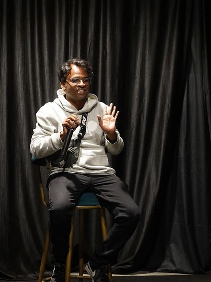 A participant shares his thoughts during a discussion or performance. The relaxed posture and engaged expression show the comfortable and interactive vibe of our events.