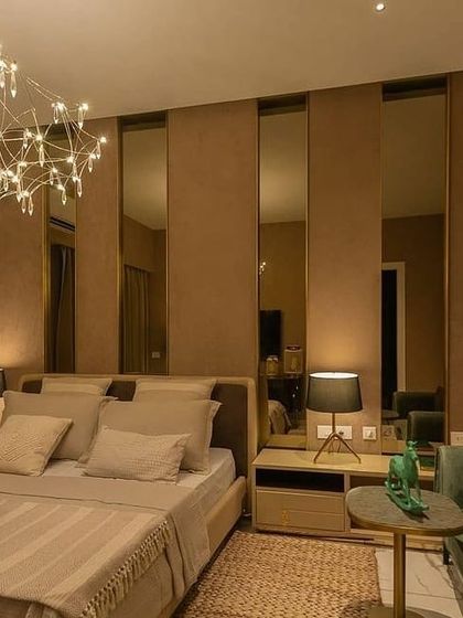 A serene bedroom where lighting creates a restful sanctuary. A delicate, artistic chandelier provides a soft, decorative glow, while small, focused bedside lamps offer perfect task lighting for reading. The layers create a warm and cozy atmosphere.