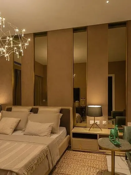 A serene bedroom where lighting creates a restful sanctuary. A delicate, artistic chandelier provides a soft, decorative glow, while small, focused bedside lamps offer perfect task lighting for reading. The layers create a warm and cozy atmosphere.