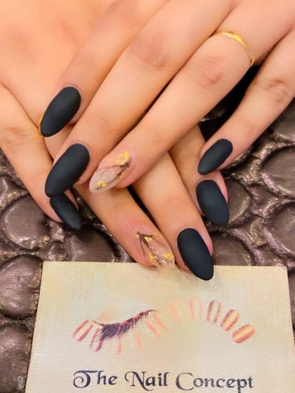 A sophisticated and moody set of matte black almond nails. The ring fingers are accented with a sheer base and a delicate design using gold foil flakes.