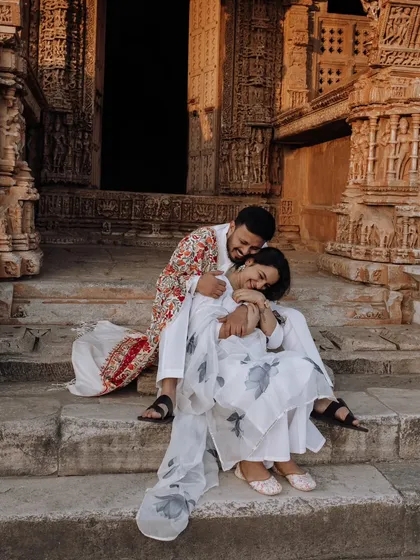 A tender and joyful moment on the steps of an ancient temple. The groom's colorful shawl adds a vibrant touch to their coordinated white outfits.