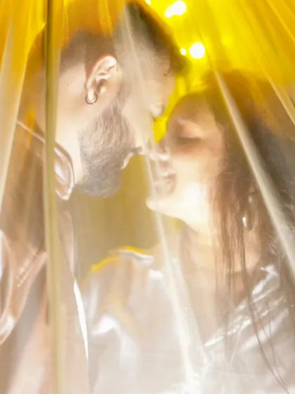 An artistic and intimate close-up shot, with the couple seen through a softly lit, translucent curtain. This creates a dreamy and romantic effect.