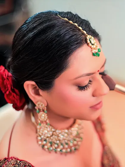 A close-up of the bride's getting-ready process, focusing on the final touches of makeup. The red rose in her hair adds a beautiful, classic detail.