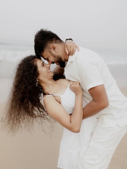 A playful and romantic moment on the beach, with a couple dancing and laughing together.