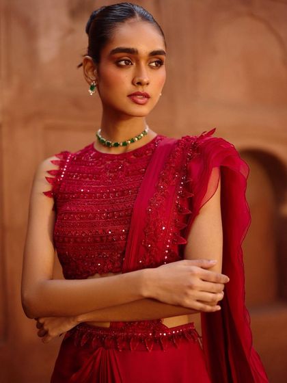 A detailed shot focusing on the craftsmanship of this red blouse. The styling is minimal, with a simple emerald choker, to let the garment's intricate embroidery and ruffled dupatta be the hero.