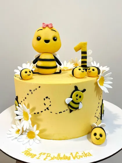 A bee-utiful cake for a first birthday! This sweet design features a bright yellow buttercream finish, fondant daisies, and adorable little bees, including a custom Cocomelon-style bee topper.