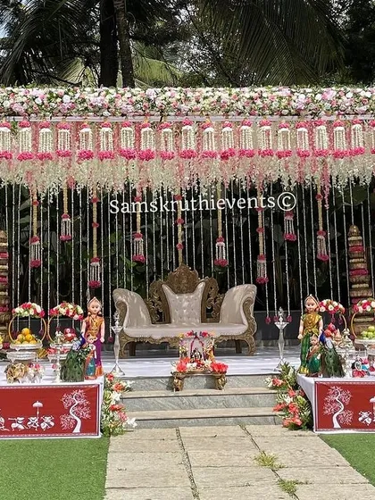 A grand outdoor baby shower setup with an elegant floral canopy. The stage is decorated with traditional dolls and offering tables, creating a luxurious and festive atmosphere.