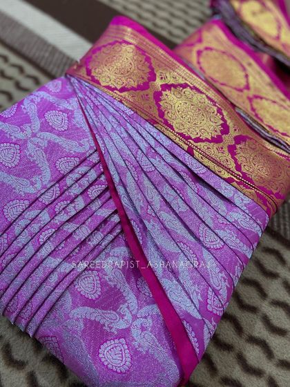 A beautiful pink and purple saree with a wide gold border, neatly box-folded. This is a perfect way to store your precious silks.
