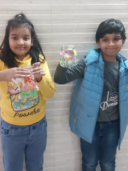 Two proud students showing off the garden-themed jars they decorated with clay. These workshops help develop fine motor skills and creativity.