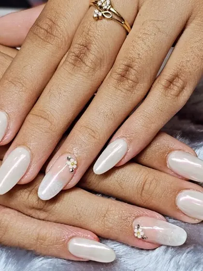 This elegant look features almond-shaped nail extensions with a pearly white chrome finish. A delicate, hand-placed floral rhinestone cluster on the accent nail adds a touch of sparkle.