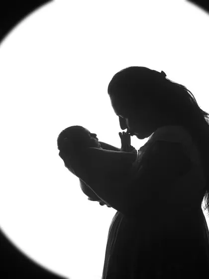 A mother's silhouette as she holds her newborn close. This style of photography creates a dramatic and emotional portrait, highlighting the deep bond between mother and child.
