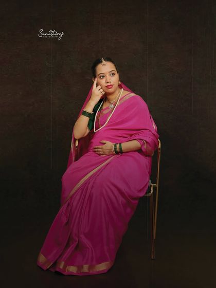 A thoughtful pose from a Ravi Varma-inspired shoot. The mother-to-be, in a pink saree, is seated on a chair, creating a classic and elegant portrait.