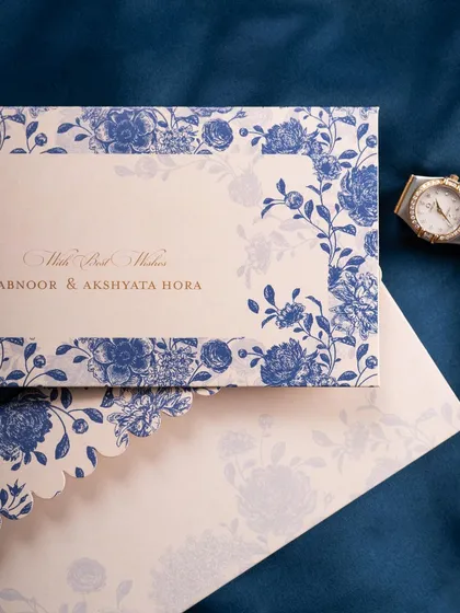 An elegant flat lay of a blue and white floral wedding invitation. The styling with a watch on a rich blue fabric gives it a personal and luxurious touch.