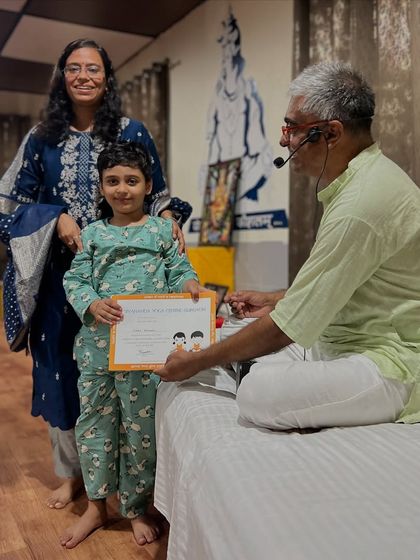 A proud moment at the Little Yogis Graduation. A young boy receives his certificate from the teacher, with his mother standing by his side.