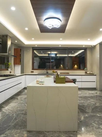 A full view of the Jains' kitchen, showing the balance between the white cabinetry, the dark marble floor, and the wood accent in the ceiling, which adds warmth to the space.