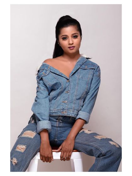 A full-length seated shot that clearly displays the ripped jeans and the overall casual-cool styling.