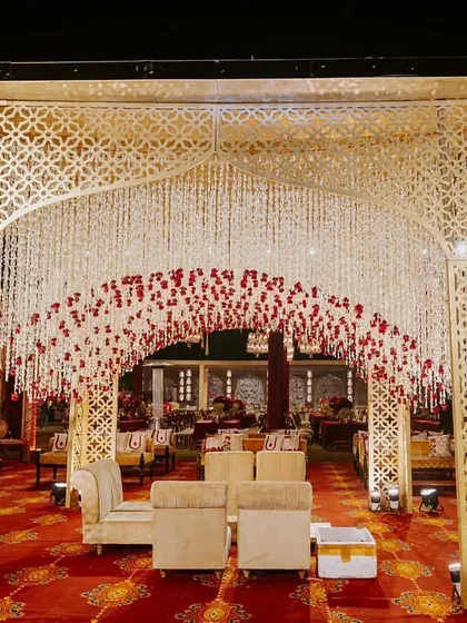 An enchanting entrance for a royal wedding, featuring a canopy of cascading white and red flowers. This design, set against the backdrop of The Leela Palace, creates a magical and opulent welcome for guests.