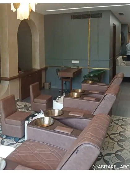 The pedicure station at a luxury salon, featuring comfortable leather chairs and elegant brass bowls. The patterned floor tiles and sophisticated color palette of grey and brown create a serene and upscale environment for relaxation.