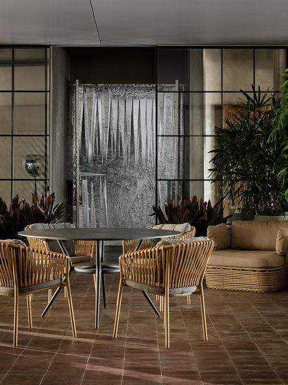 An outdoor furniture setup, complete with woven dining chairs and a sofa. This zone is designed to show customers how the pieces would look on a patio or terrace, complete with a water feature in the background.