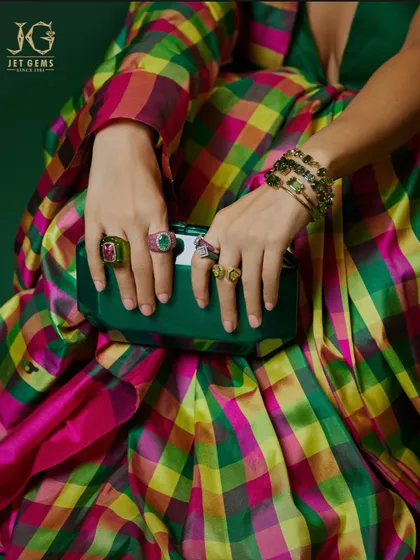 A close-up of Bhumi Pednekar's hands, showcasing a stunning collection of my bold gemstone rings in emerald and ruby, perfectly complementing her vibrant outfit and clutch.