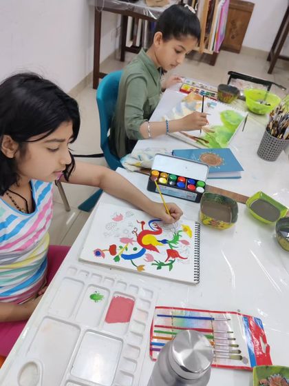 A young student learns a traditional Indian folk art style, carefully painting vibrant, stylized birds and flowers.