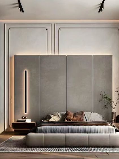 A minimalist bedroom design with a serene and calming atmosphere. The focal point is a tall, grey upholstered headboard, complemented by classic wall molding and a sleek, glass-doored wardrobe.