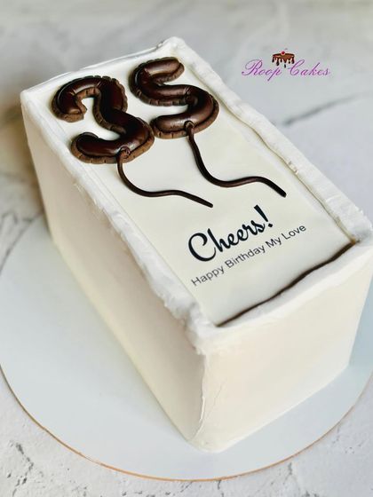 A toast to 35. This sleek, rectangular cake features edible, balloon-shaped numbers and a simple "Cheers! Happy Birthday My Love" message, perfect for a modern and stylish celebration.