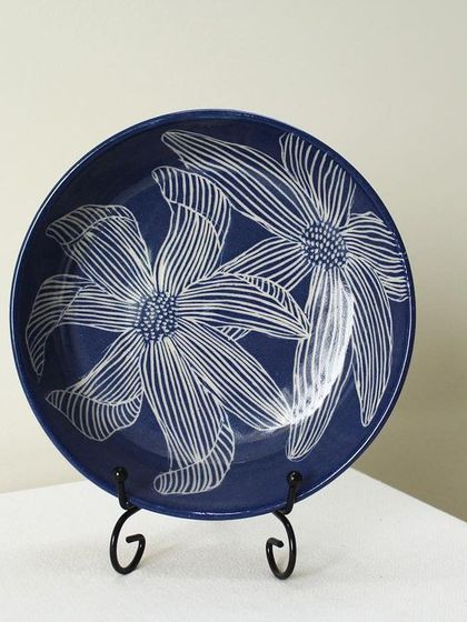 My Dutch Iris pasta bowl displayed as a piece of decorative art. The intricate, hand-carved floral pattern stands out against the deep indigo blue, making it a statement piece.