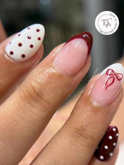 A close-up of a playful Christmas manicure, showing the detail of the hand-painted bow and the crisp polka dots.