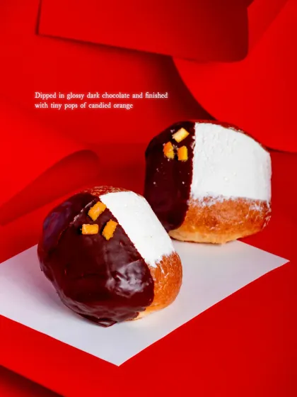 A pair of Dark Chocolate Orange Maritozzi, showing the glossy dark chocolate dip and pops of candied orange. They are as beautiful as they are delicious.