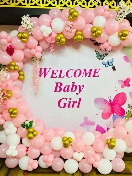 A sweet butterfly-themed backdrop to welcome a baby girl. The design uses a pink and white balloon arch with gold accents and delicate butterfly stickers.