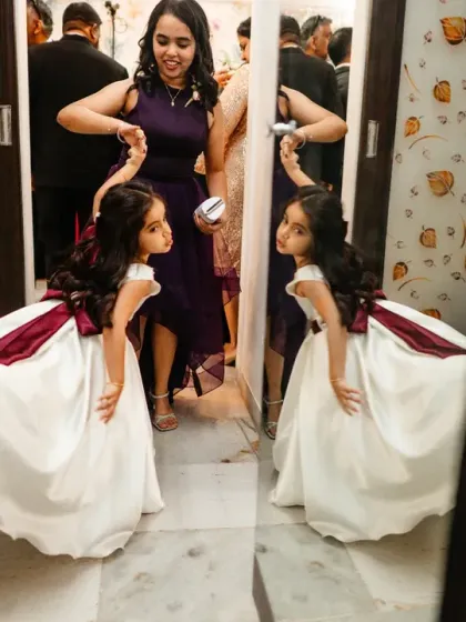 A flower girl discovers her reflection in the mirror, a moment of pure childhood wonder.