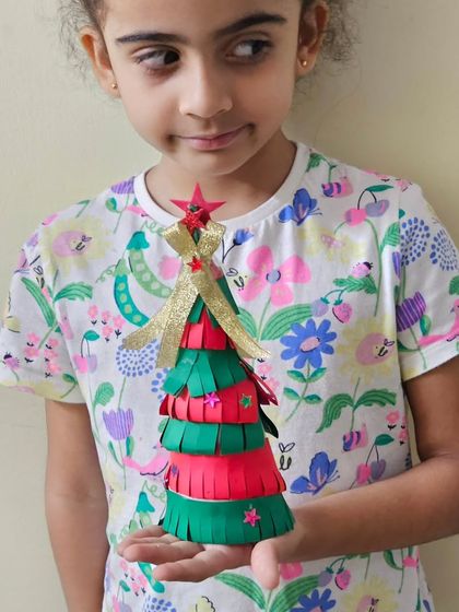Jingle bells and artistic skills! A student proudly holds up a 3D paper Christmas tree she crafted during our holiday workshop.