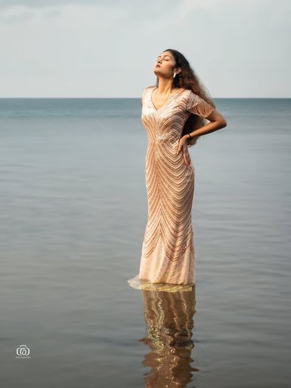 A powerful and serene image of a model standing in the ocean in a full-length gown. The reflection in the water and the vastness of the sea create a truly epic and cinematic shot.