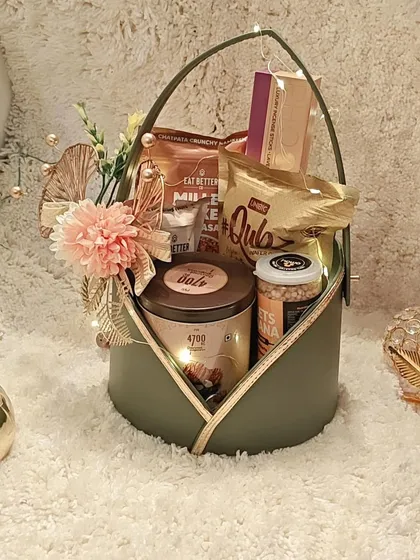 A still shot of the elegant olive green basket, showcasing items like 4700BC popcorn, cookies, and luxury incense sticks.
