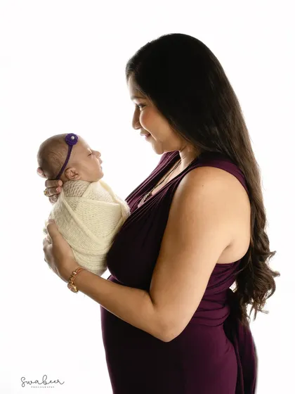 A mother gazes lovingly at her newborn, a simple and powerful moment of connection. The clean white background keeps the focus entirely on their bond.