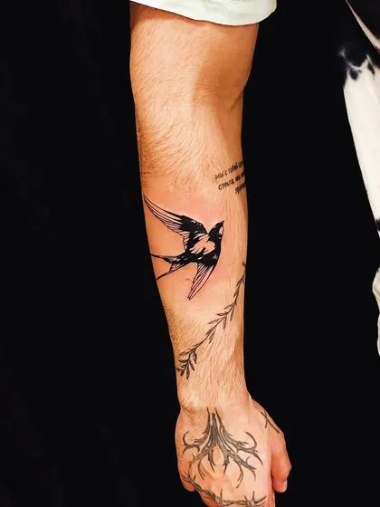 A detailed swallow tattoo on the forearm, with additional branch and root designs on the hand, creating a larger nature-themed composition.