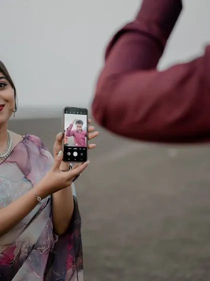A fun, meta photograph where the bride holds up a phone showing a picture of the groom. This creative and playful concept adds a modern and personal touch to their beach shoot.