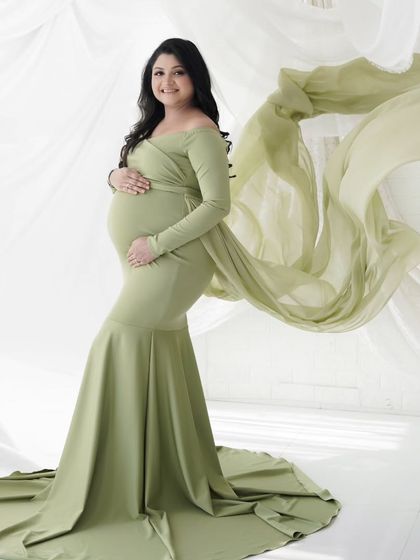 The flowing fabric of this green gown adds a touch of grace and movement to this solo maternity portrait, taken against a clean white backdrop in the studio.